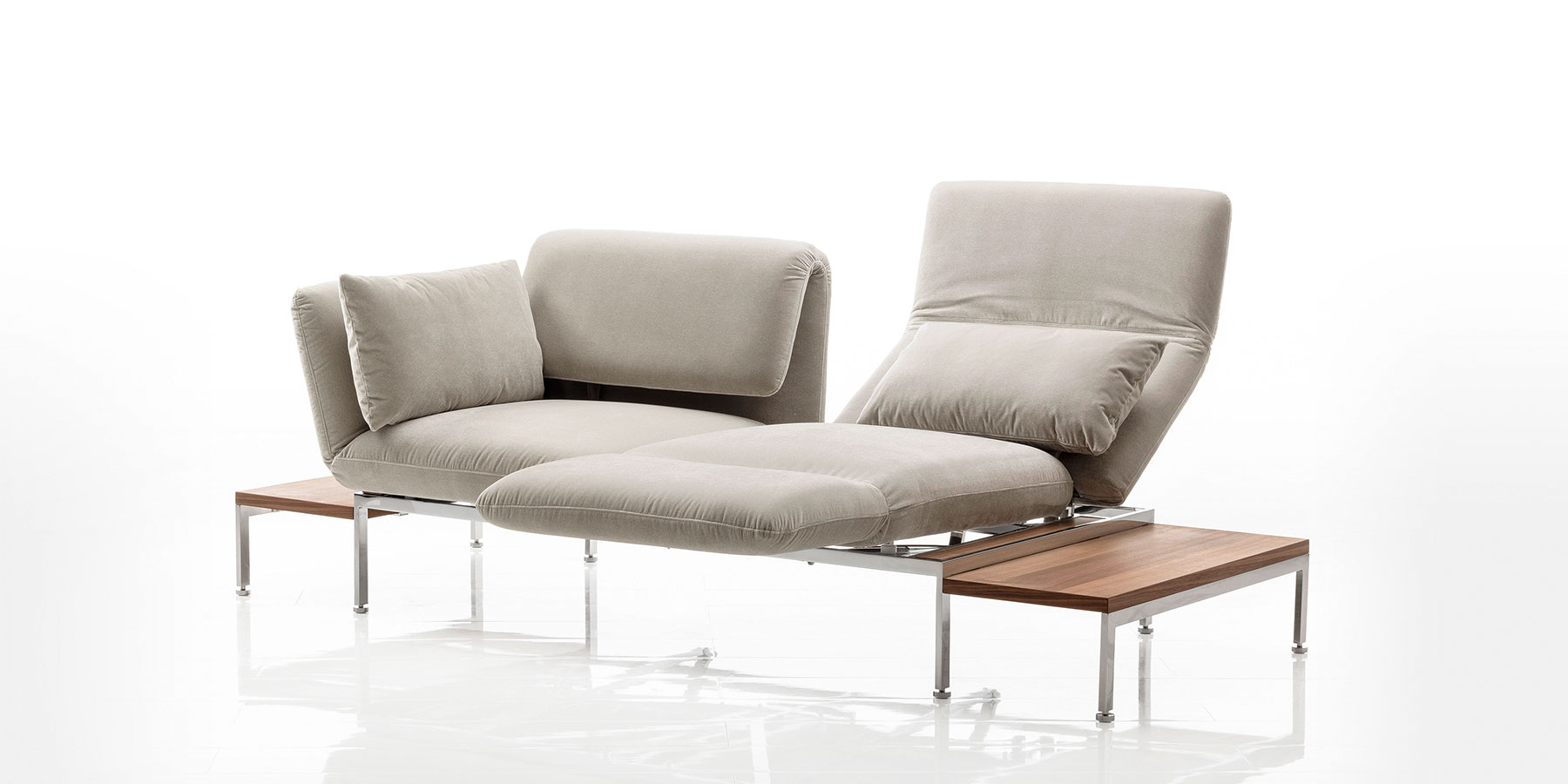 Ein zweisitziges Sofa mit Andocktischen rechts und links. Am rechten Sitzplatz wurde die Armlehne zur Fußstütze umgeschwenkt, um eine Relaxposition herzustellen.