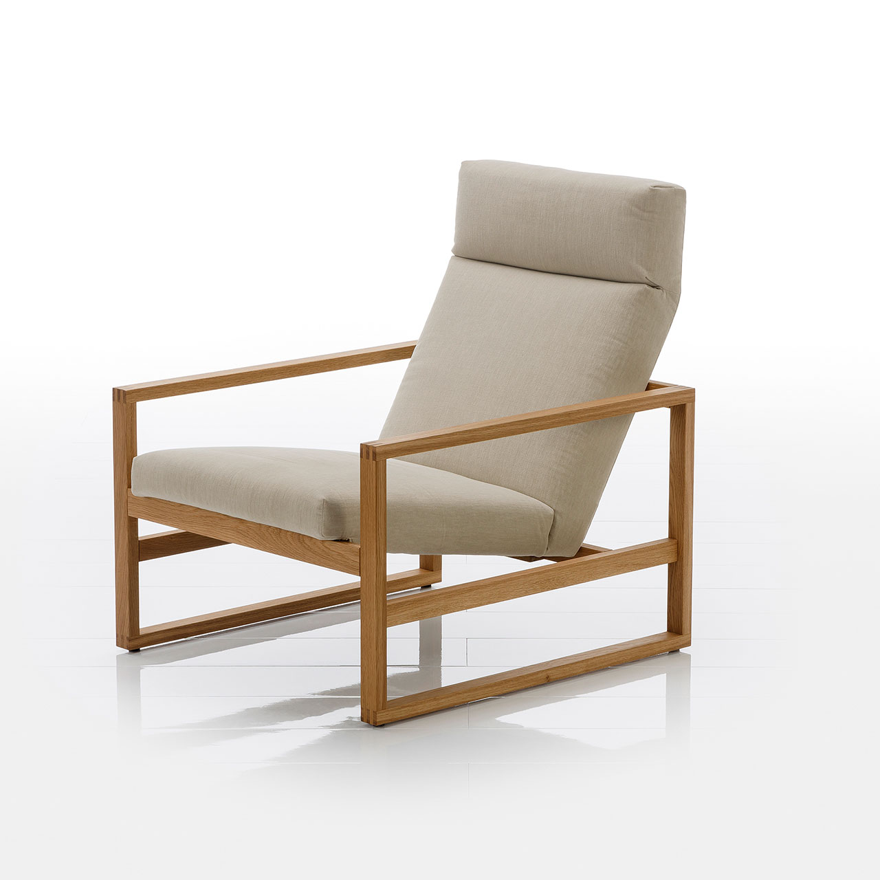 Schräge Sicht auf einen niedrigen Lounge-Sessel mit Holzgestell in heller Eiche. Die Sitzfläche ist mit hellbeigem Stoff bezogen.