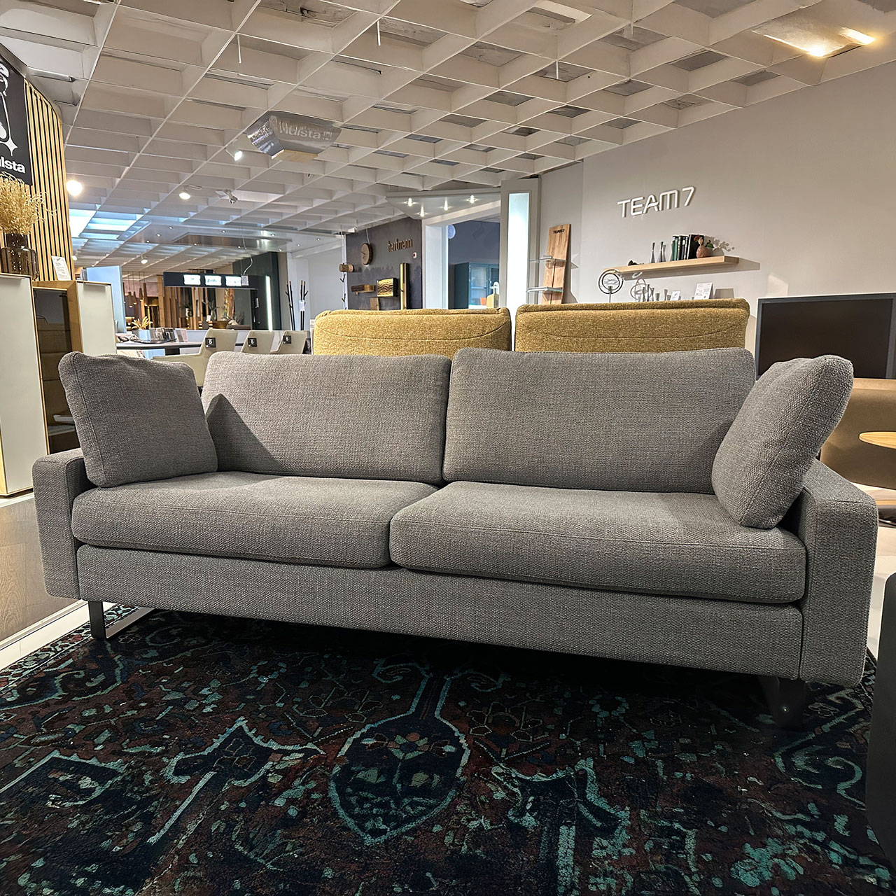 Zweisitzer mit niedriger Armlehne und zwei Kissen im gleichen grauen Stoff wie der Bezug.