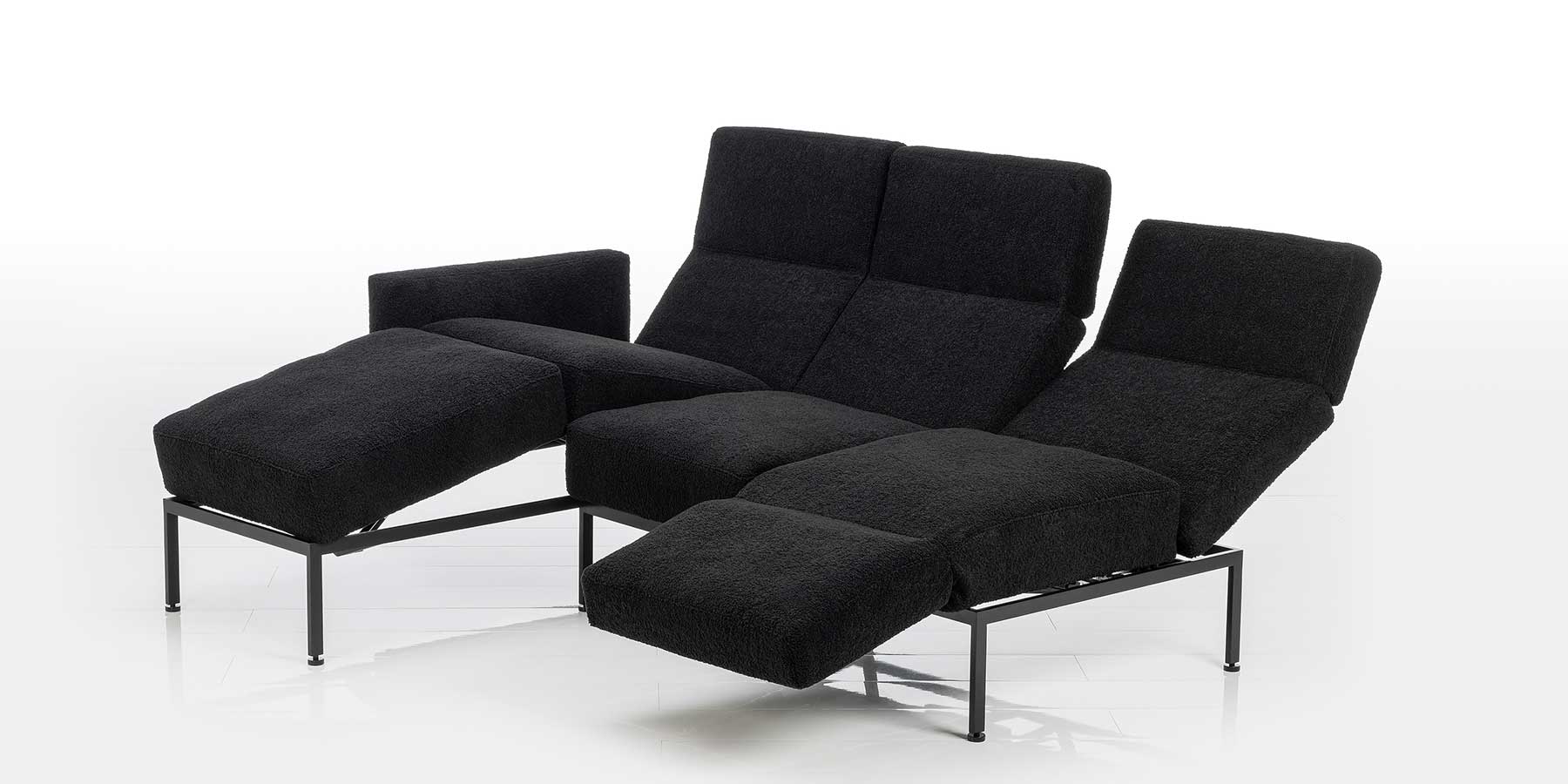 Kombination aus Longchair und Anstellsofa in schwarzem Stoff. Die Sitzplätze sind in verschiedene Relaxpositionen eingestellt. 