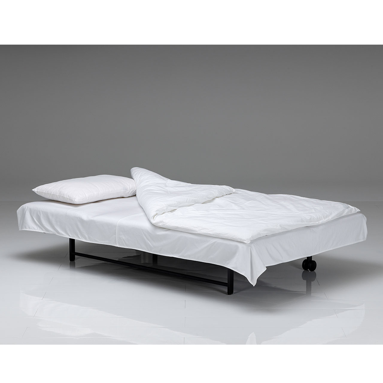 Zu einer Liegefläche umgeklapptes Bettsofa. Das Gästebett ist mit einem weißen Laken  bezogen. Am Kopfende liegt ordentlich ein weißes Kopfkissen, die ebenfalls weiße Bettdecke ist ausgebreitet und aufgeschlagen.