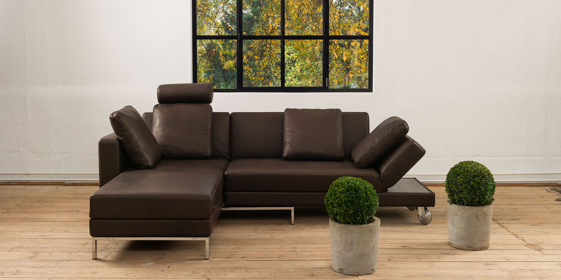 Eine Eckgarnitur in braunem Leder mit chromfarbenen Füßen. Links mit einem Openend, rechts mit einem Anstellsofa mit halb abgesenkter Armlehne.