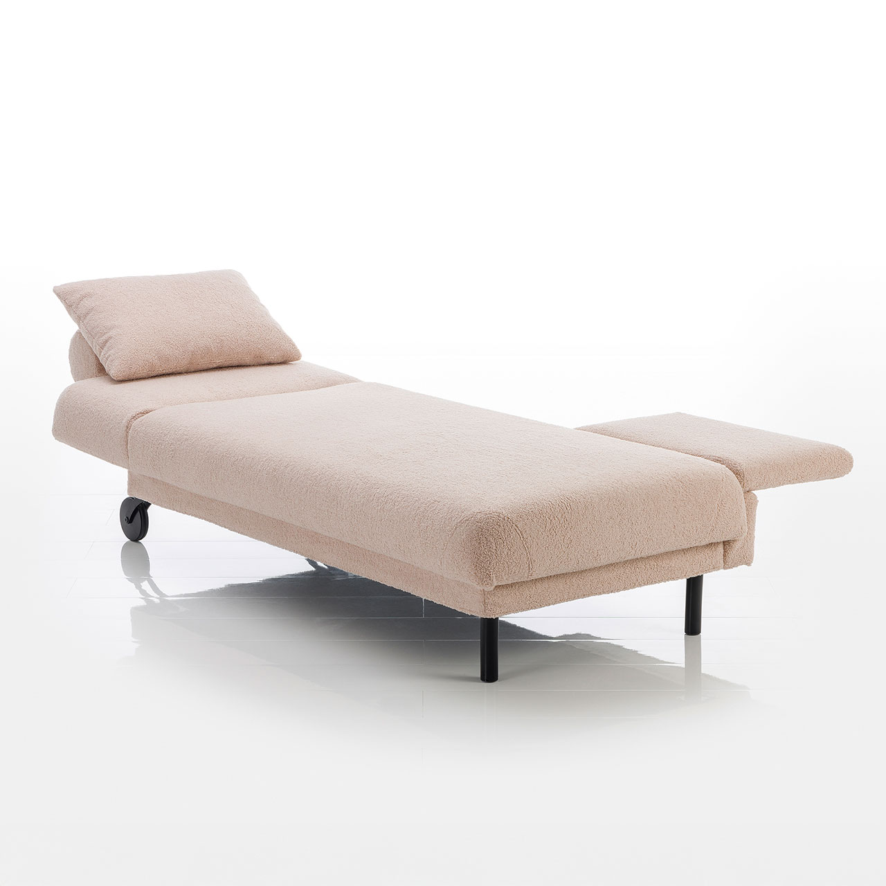 Recamiere in hellbraunem Stoff mit Rollen an der Kopfseite und zylindrischen Füßen an der Fußseite. Mit höhenverstellbarem Kopfteil und verschiebbarer Armlehne links.