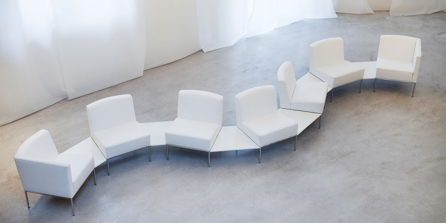 Sieben weiße Sessel von brühl add1 sind mit Ablagen schlangenlinienförmig miteinander verbunden.