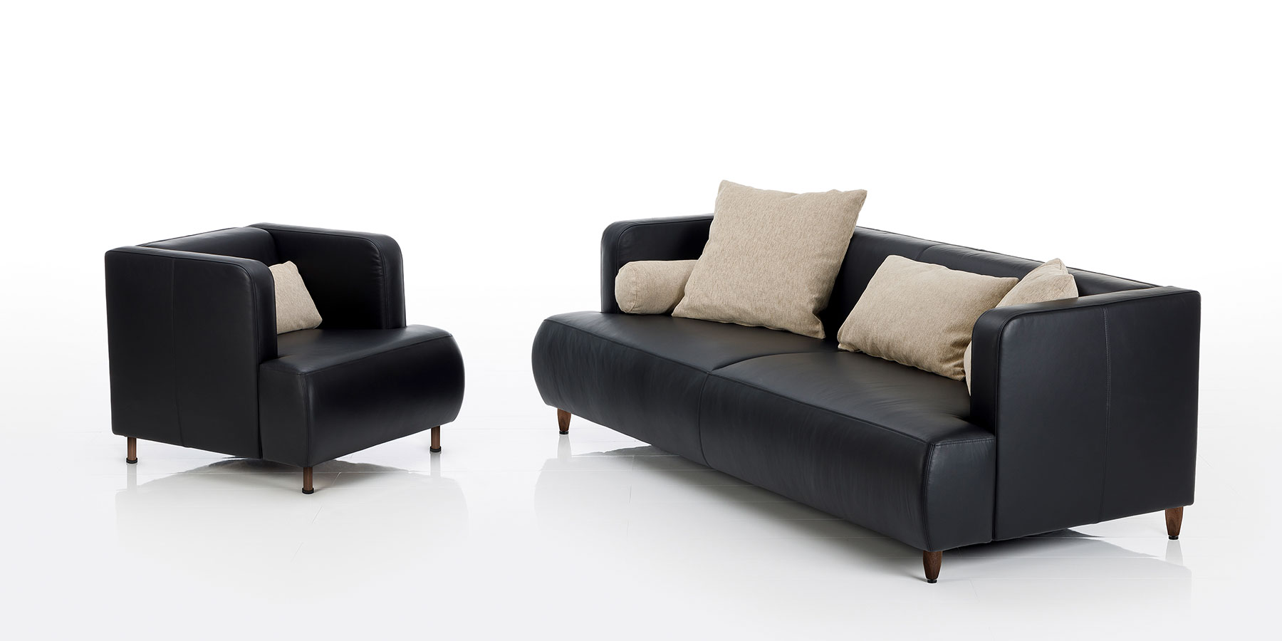 Ein Ledersessel und eine Ledercouch von brühl aoyama aus schwarzem Leder mit Dekokissen in beige.