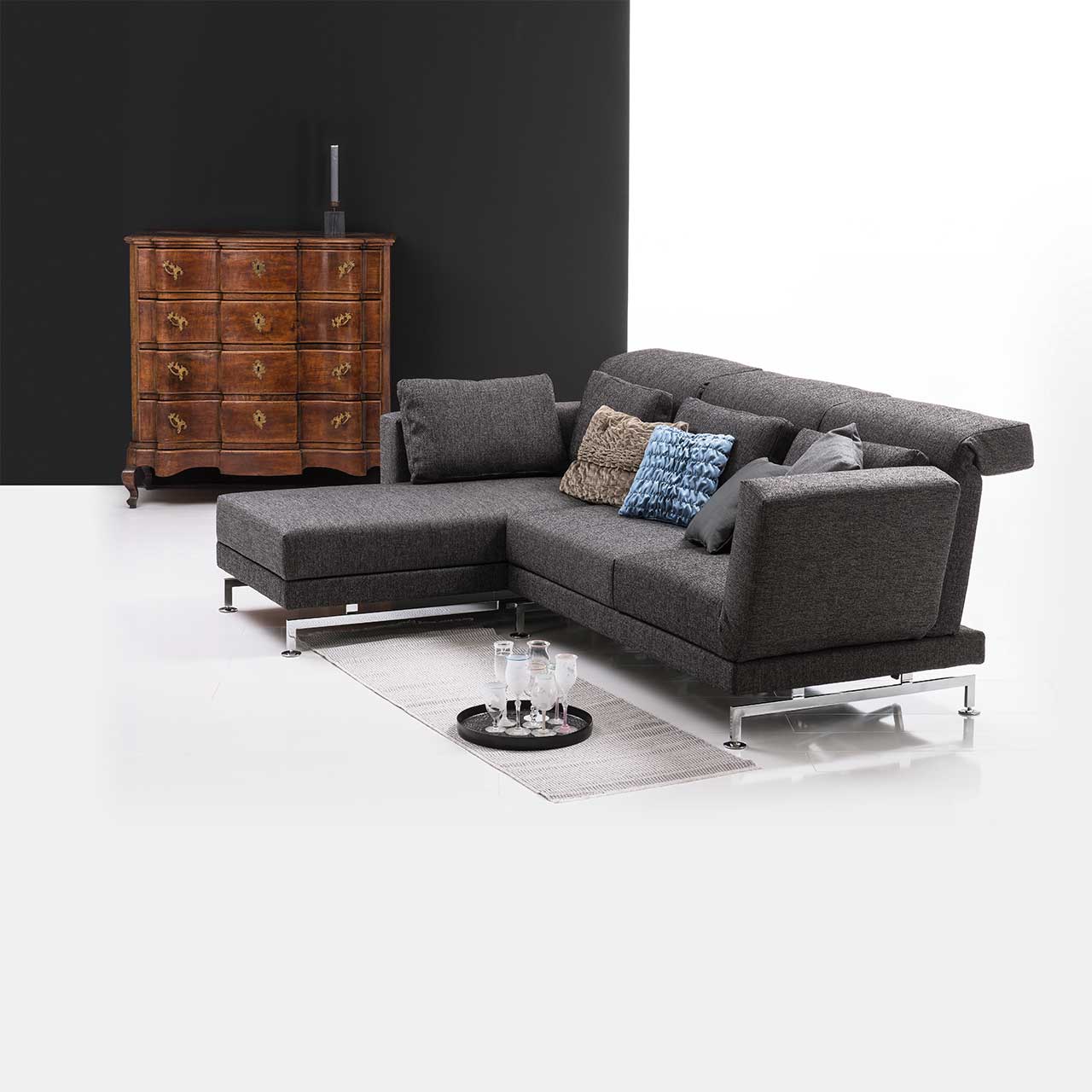 Eckgarnitur in grauem Stoff mit Longchair links, dekoriert mit bunten Kissen.