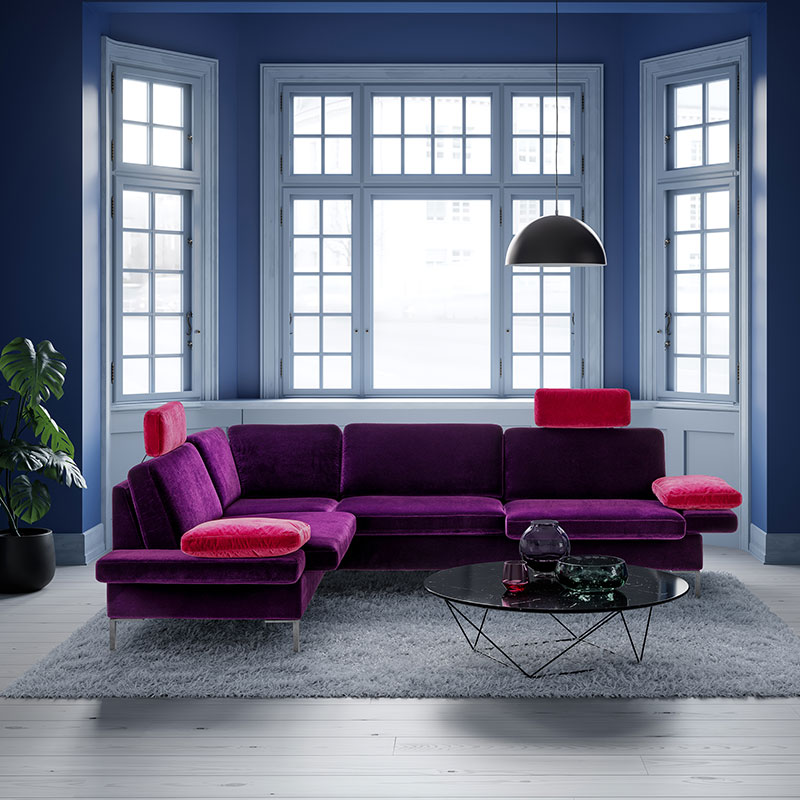 Ambientebild mit lila-pinker Eckgarnitur vor einem großen Fenster.